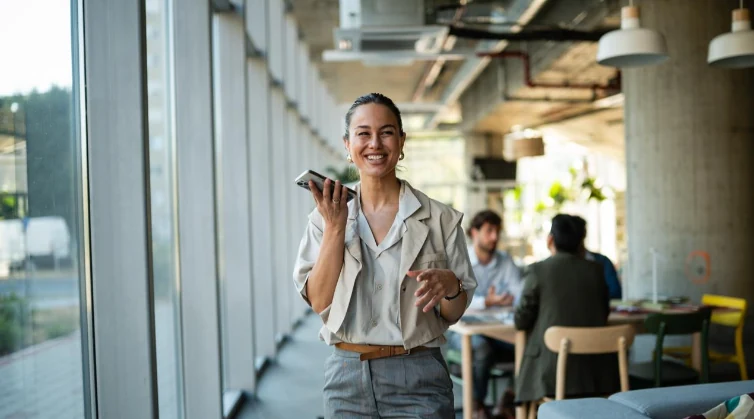 Young professional walking through an office hall, smiling and talking into her phone