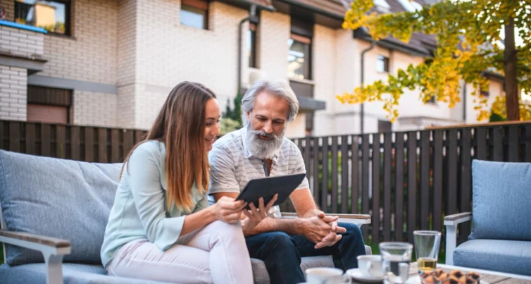 Father and adult daughter looking at a tablet together on a terrace